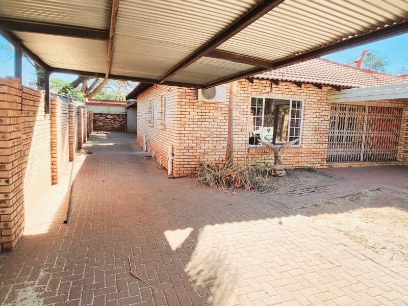 Exterior view of the property featuring a paved driveway, a covered carport, and brick facade with security gates.