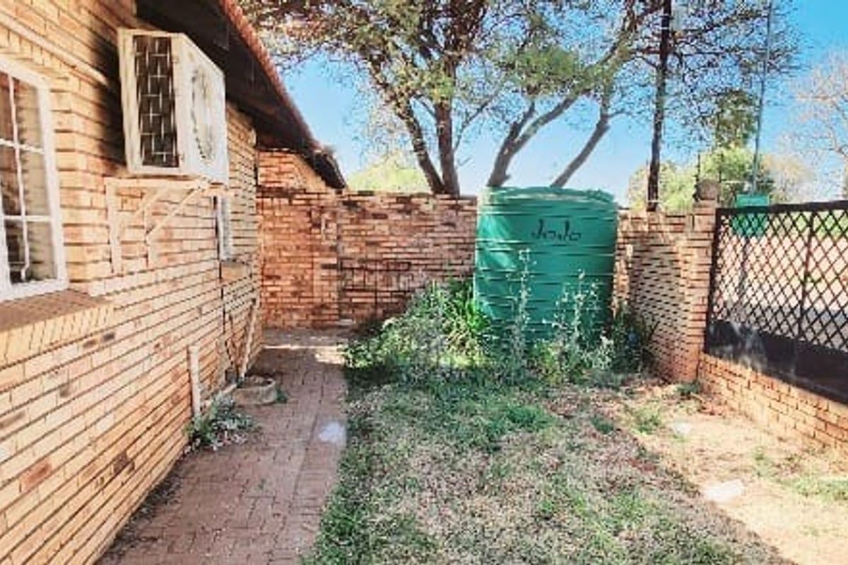 A rear exterior view of the property featuring a brick facade, paved walkway, water storage tank, and enclosed garden area with perimeter walling.