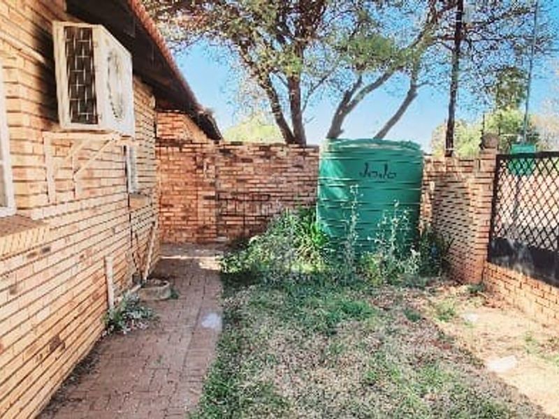 A rear exterior view of the property featuring a brick facade, paved walkway, water storage tank, and enclosed garden area with perimeter walling.