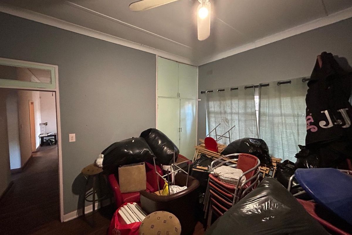 A bedroom featuring built-in cupboards, a ceiling fan, and timber flooring, currently used for storage.