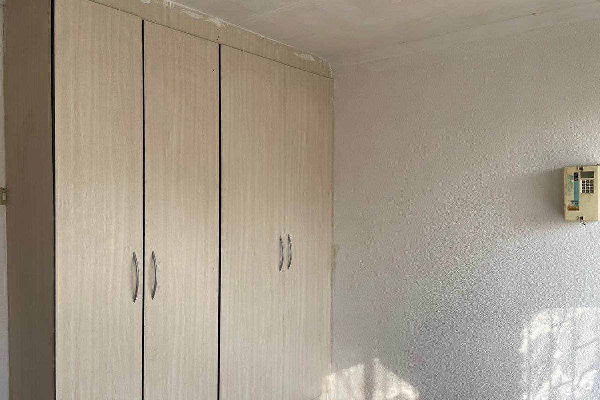 A bedroom featuring built-in light wood-grain wardrobes and a wall-mounted security alarm panel, requiring minor cosmetic repairs to the ceiling and walls.