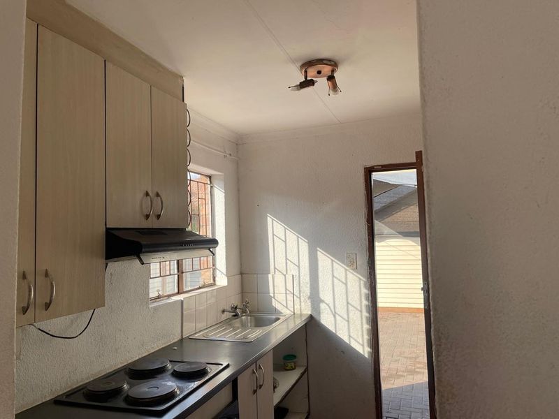 Compact kitchen featuring built-in cabinetry, an electric hob with extractor fan, and a stainless steel sink, with direct access to the exterior.
