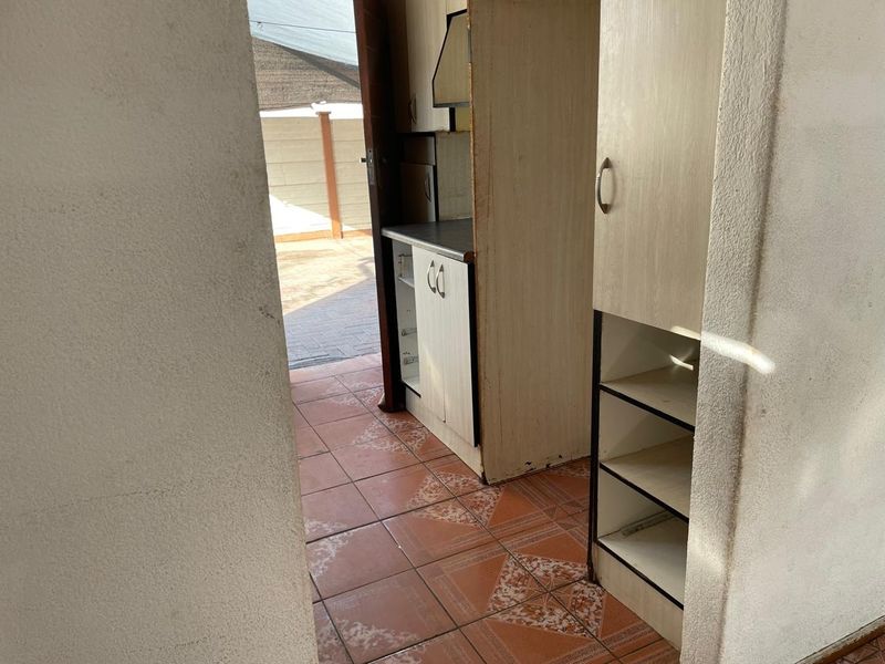 A compact scullery or utility area featuring built-in cabinetry, tiled flooring, and an extractor fan, providing functional prep space with direct outdoor access.
