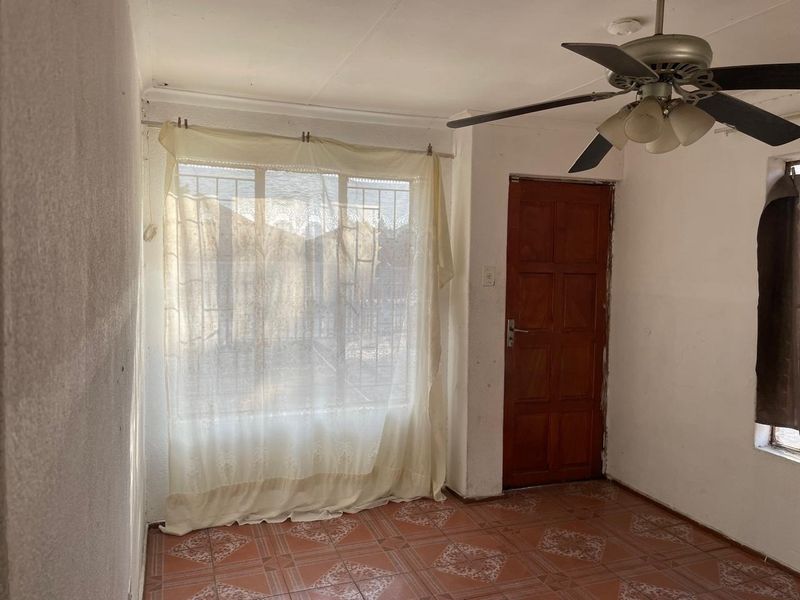 An empty living area featuring tiled flooring, a ceiling fan, and a timber door with access to the exterior.
