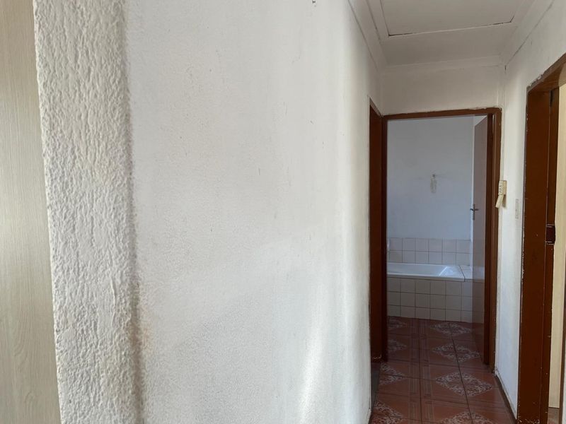 A narrow hallway with tiled flooring leading into a bathroom featuring a built-in bathtub.
