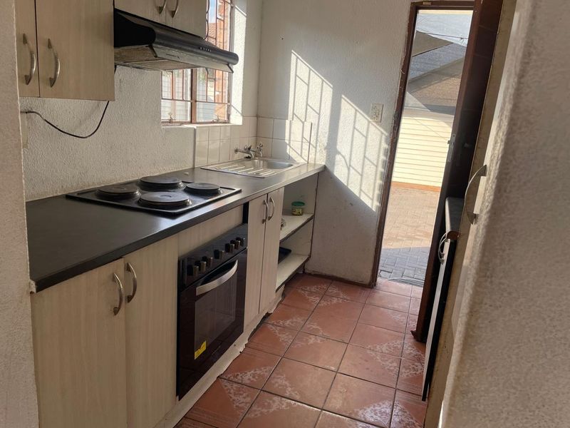 Compact kitchen featuring built-in cabinetry, electric hob, oven, extractor fan, and direct access to the rear exterior area.