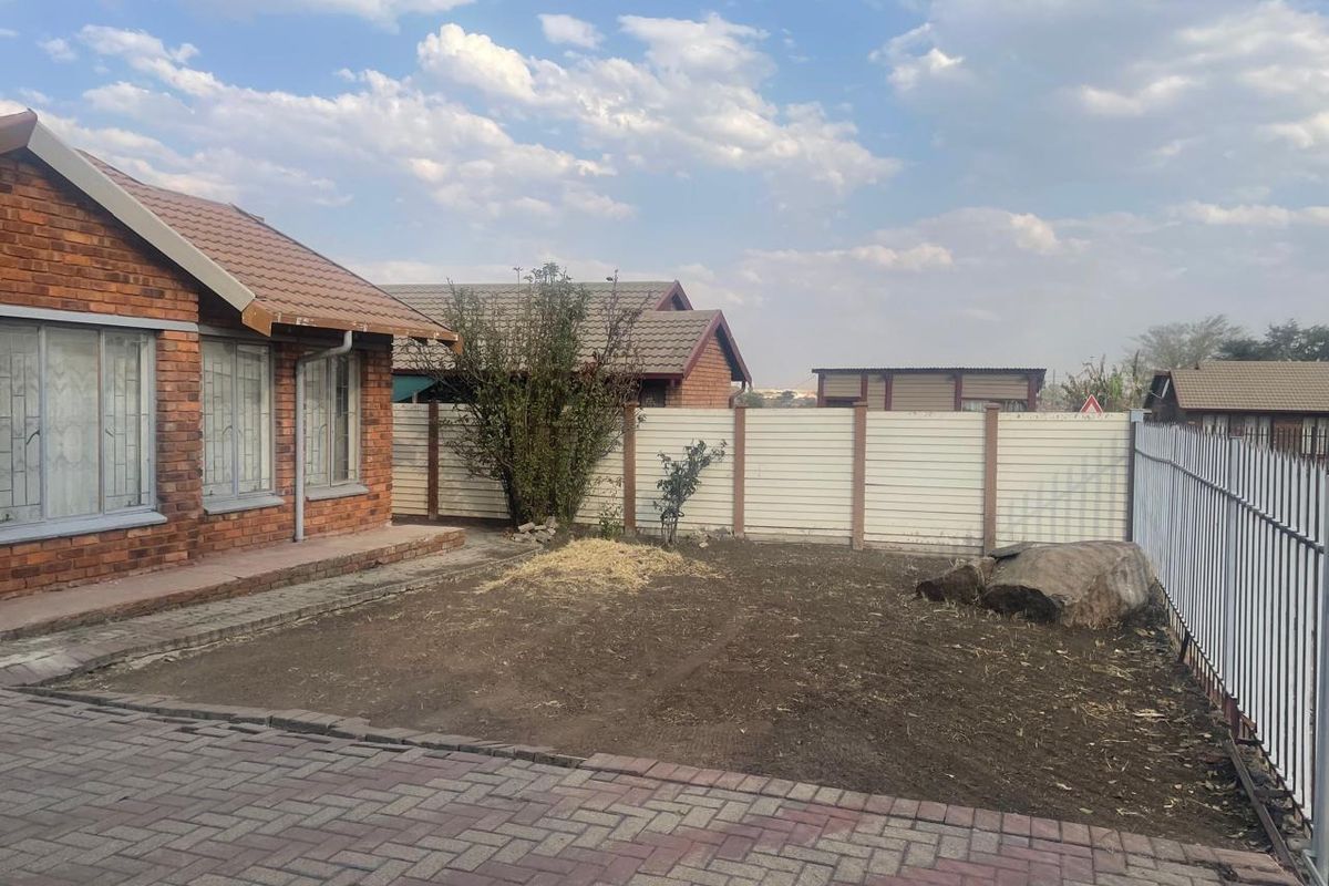 A rear exterior view of a face brick house featuring a paved area and an unlandscaped garden enclosed by precast and metal fencing.