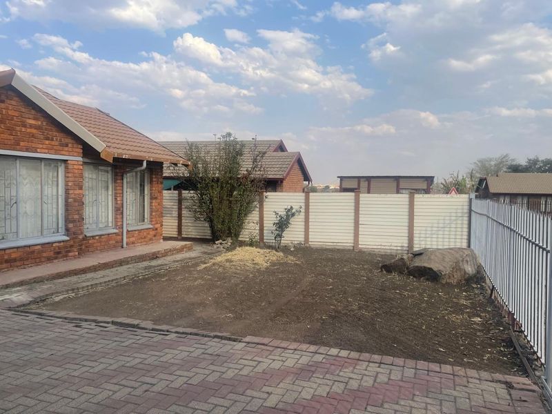 A rear exterior view of a face brick house featuring a paved area and an unlandscaped garden enclosed by precast and metal fencing.