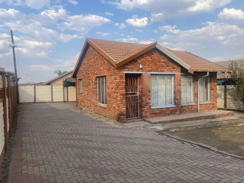 A well-maintained face brick house featuring a tiled roof, paved driveway, and secure entrance, set within a fenced property.