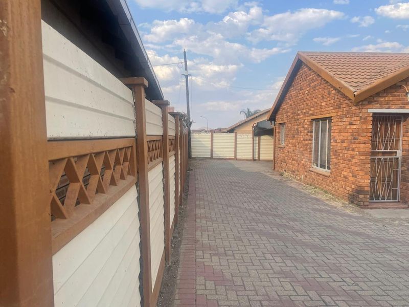 A side view of a face brick house featuring a paved driveway and a secure precast concrete boundary wall.