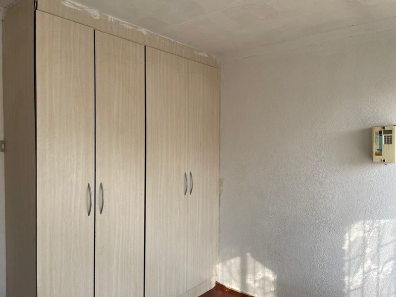 A bedroom featuring built-in wooden cupboards and an alarm system, requiring cosmetic attention to the ceiling and wall finishes.