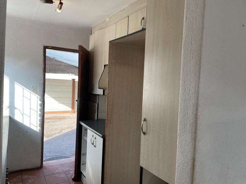 A compact kitchen area featuring built-in cabinetry, laminate countertops, and an extractor fan, with direct access to an outdoor paved area.