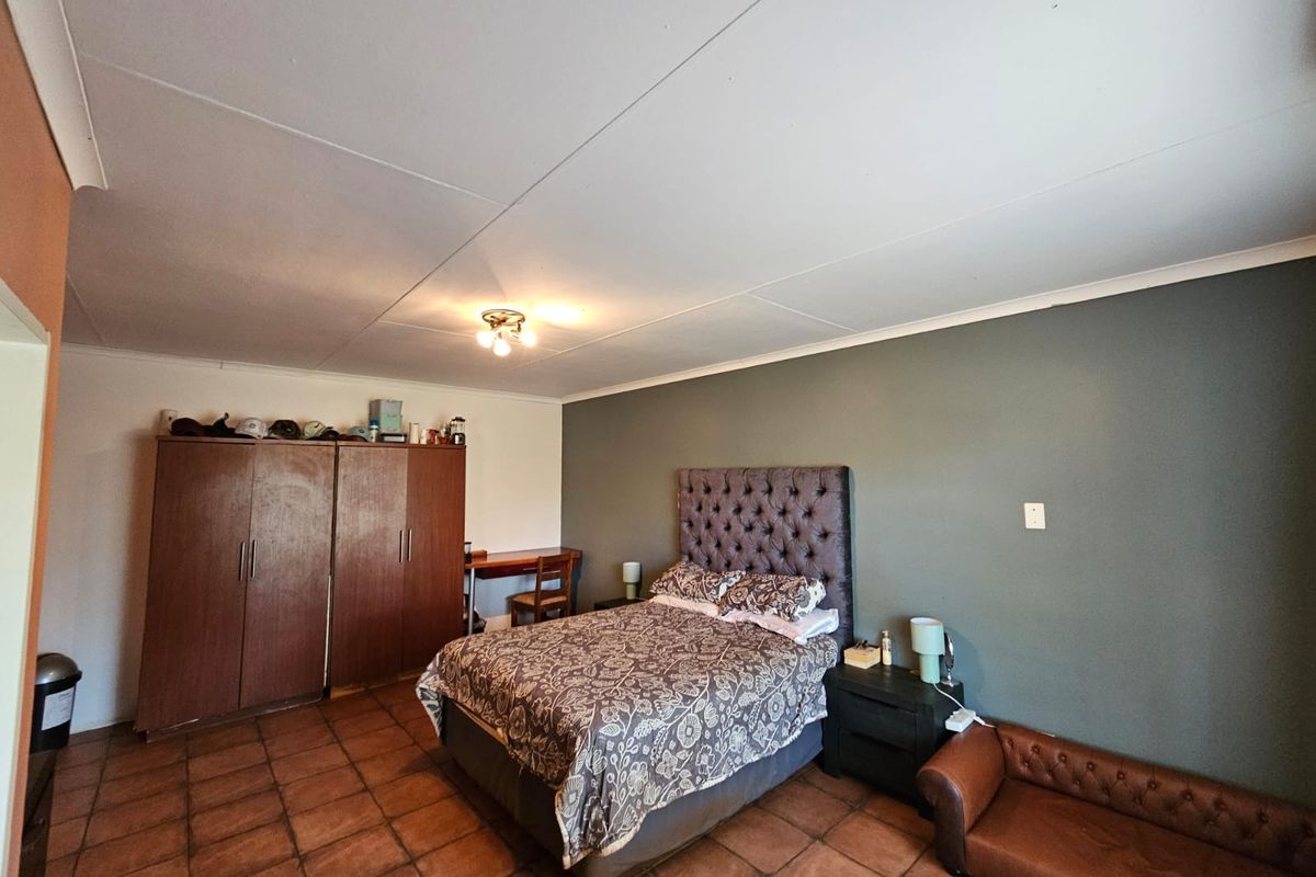 A spacious bedroom featuring tiled flooring, a neutral color palette with an accent wall, and built-in wooden cabinetry.