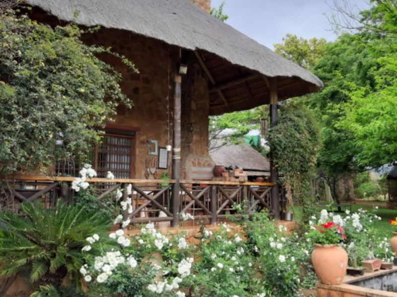 A charming rustic farmhouse featuring a traditional thatched roof, stone masonry walls, and a covered wooden veranda overlooking a landscaped garden.