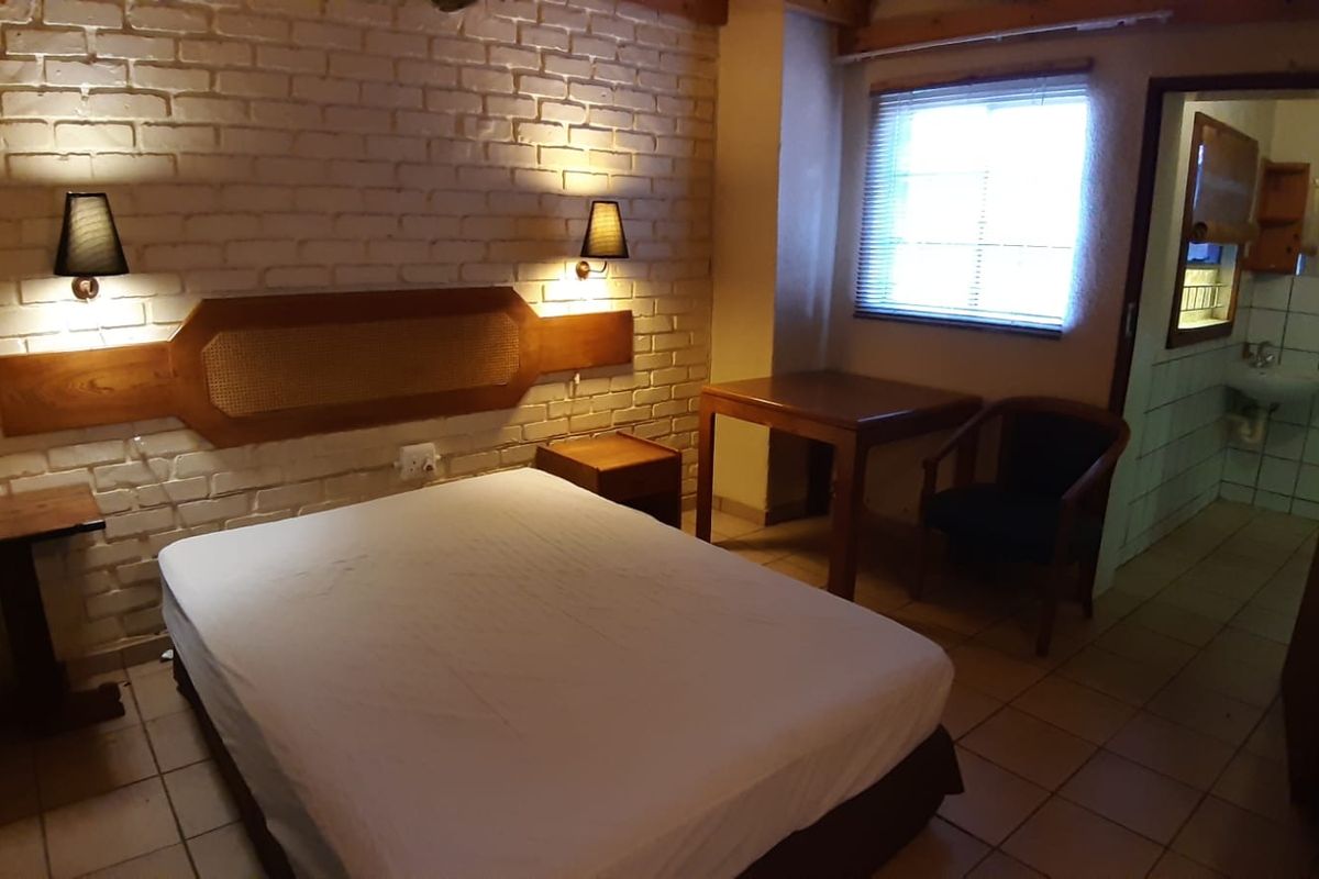 A rustic bedroom featuring exposed brick walls, tiled flooring, and an en-suite bathroom, offering a cozy and functional living space.
