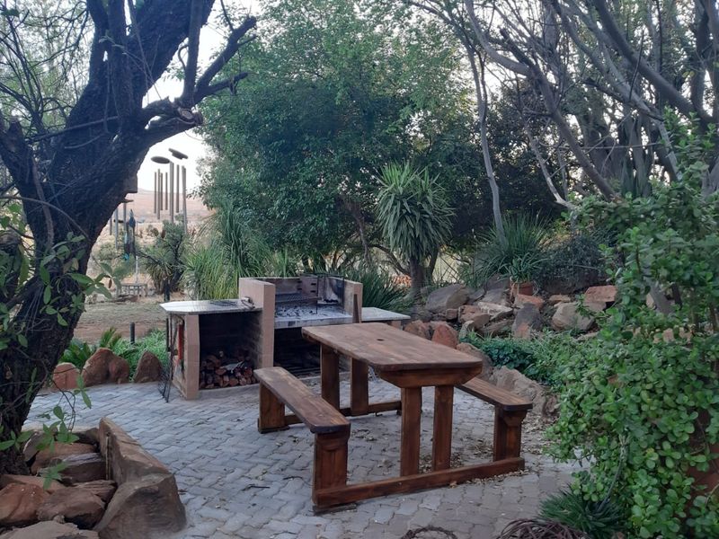 Outdoor entertainment area featuring a built-in brick braai and paved patio set within a natural, landscaped garden environment.