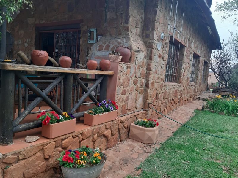 A rustic stone-clad farmhouse exterior featuring a covered patio area with timber railings and a thatched roof profile.