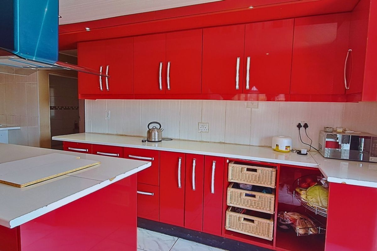A vibrant kitchen featuring high-gloss red cabinetry, a central island with a white countertop, and a modern stainless steel extractor fan.