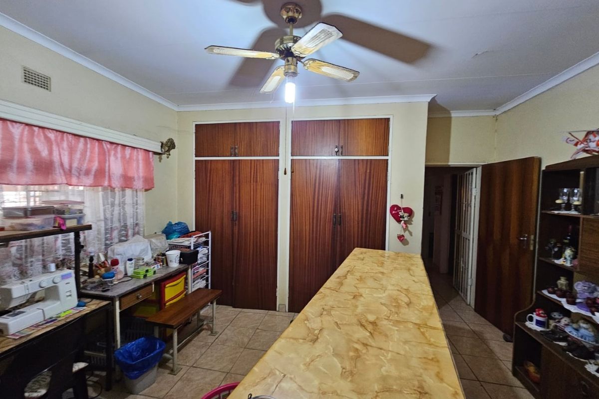 A functional room featuring built-in wooden cupboards, a central ceiling fan, and tiled flooring, offering versatile space for storage or utility use.