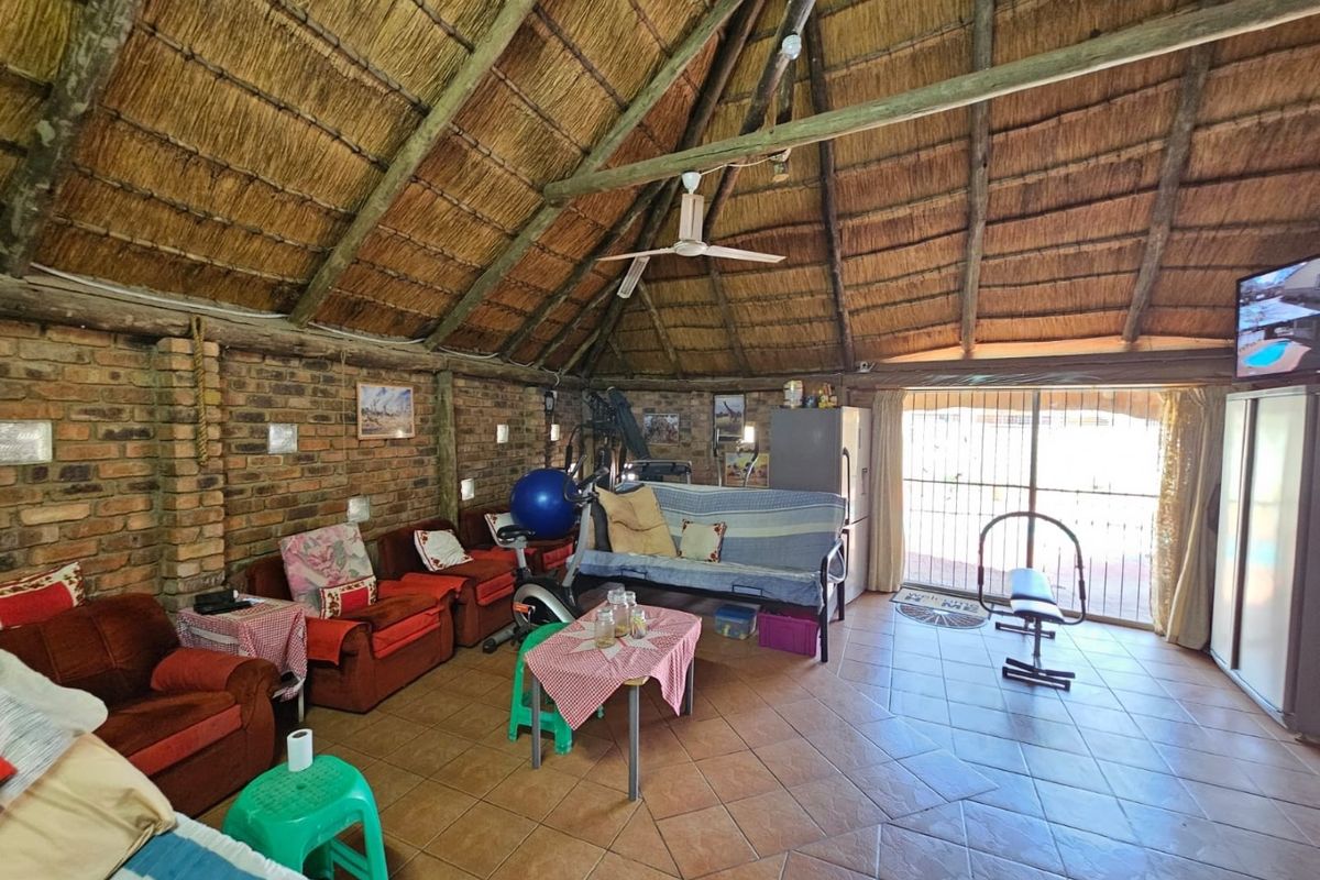 Spacious living area featuring a high vaulted thatched ceiling, exposed brick walls, and tiled flooring with direct access to the outdoor patio area.