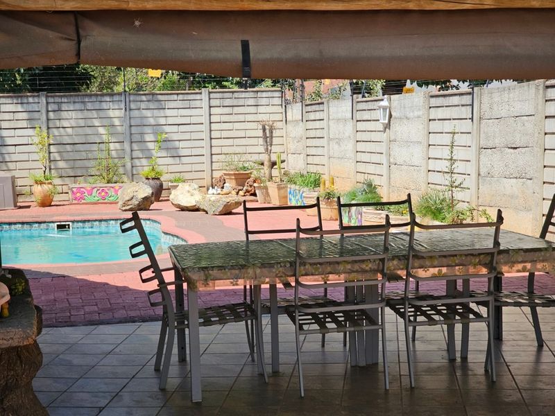 Covered patio area overlooking a swimming pool and garden, featuring tiled flooring and a secure concrete boundary wall.