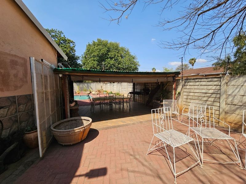 Outdoor patio area featuring a covered entertainment space, brick paving, and direct access to the swimming pool and garden area.