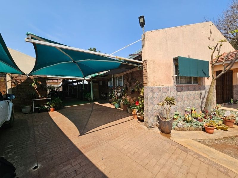 Exterior view of the property featuring a paved driveway, a large shade sail structure, and established garden beds along the building facade.