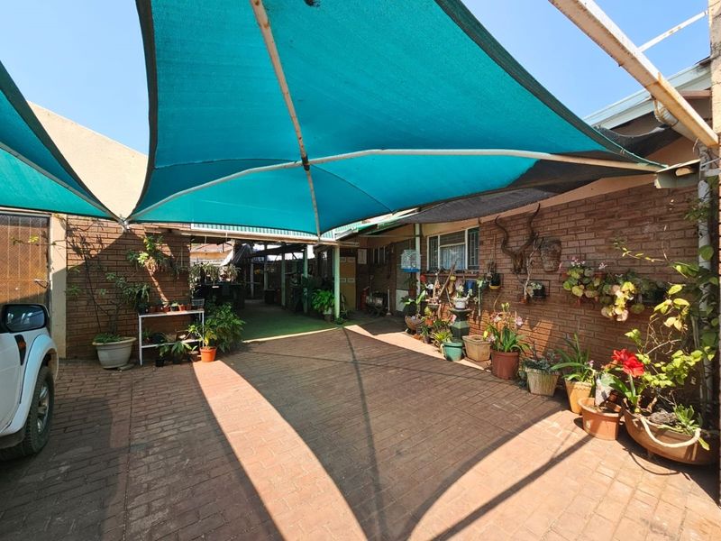 A paved outdoor patio area featuring a large teal shade sail, brick wall construction, and direct access to the home's exterior.
