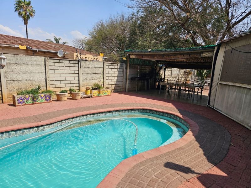 Outdoor pool area featuring a paved deck, a covered patio entertainment space, and a perimeter boundary wall.