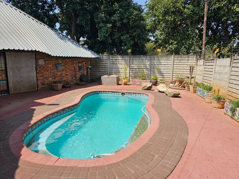 Outdoor pool area featuring a kidney-shaped swimming pool, paved surround, and perimeter walling, set against a backdrop of mature trees.