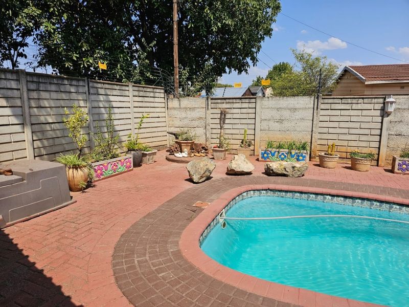 Outdoor pool area featuring a paved patio, swimming pool, and precast concrete boundary wall with security fencing.