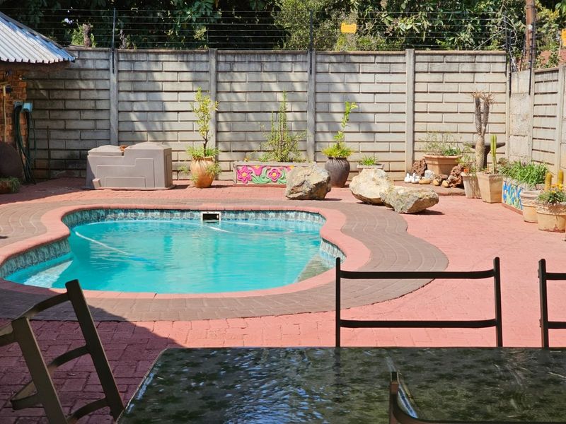 Outdoor pool area featuring a paved patio, swimming pool, and high boundary wall with electric fencing.