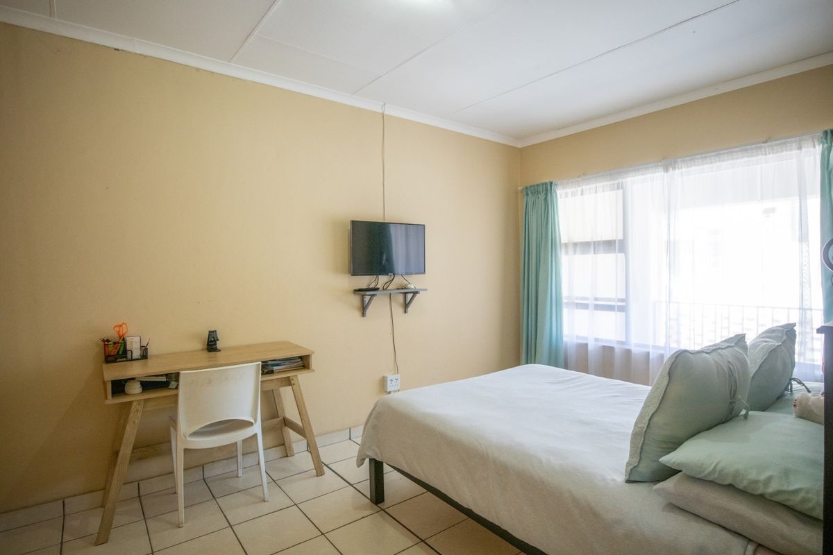 A functional bedroom featuring tiled flooring, large window with natural light, and neutral wall finishes, suitable for a comfortable living space.