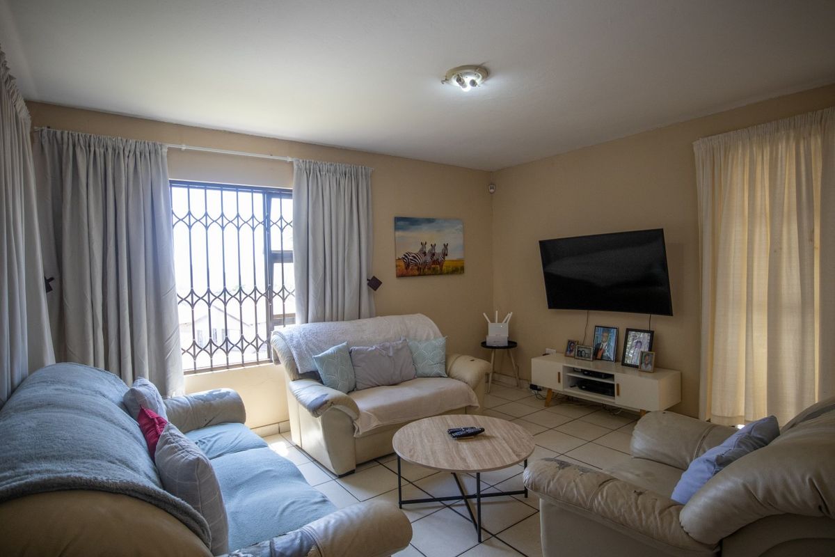 A comfortable living room featuring tiled flooring, security bars on the window, and neutral wall finishes.