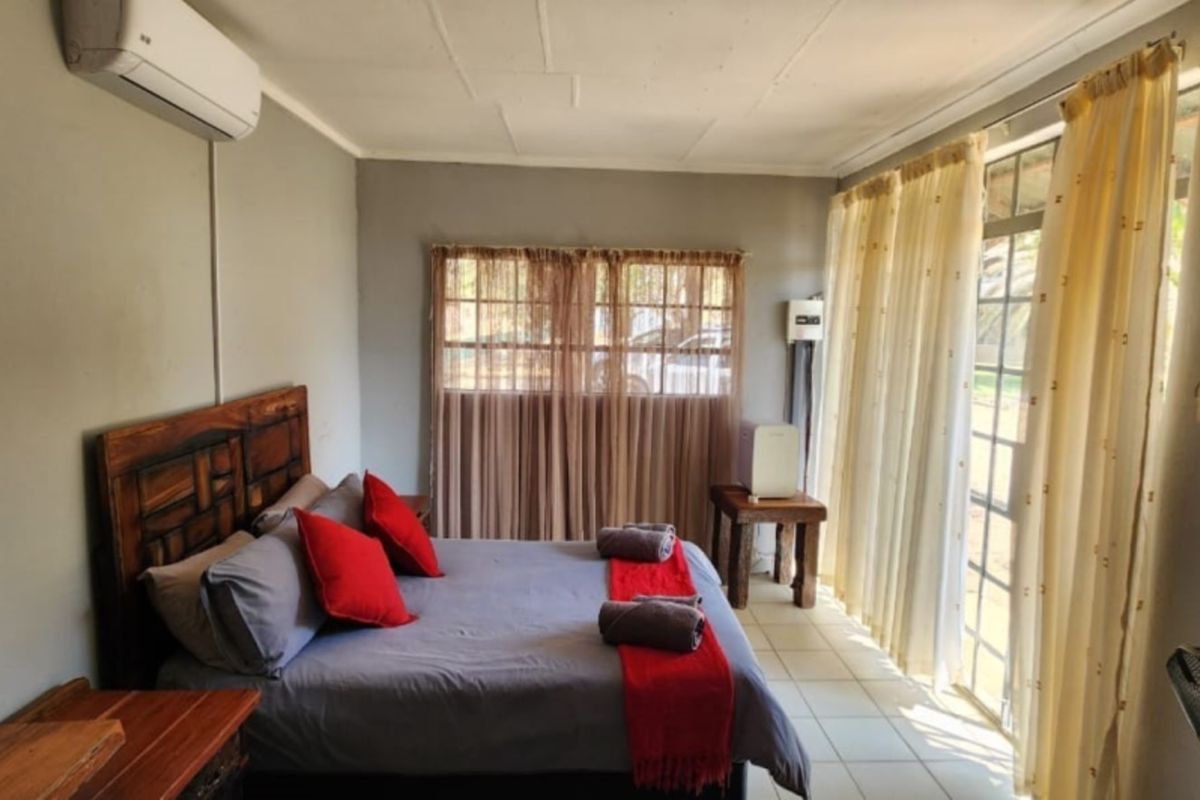 A functional bedroom featuring tiled flooring, a wall-mounted air conditioning unit, and large windows providing natural light.