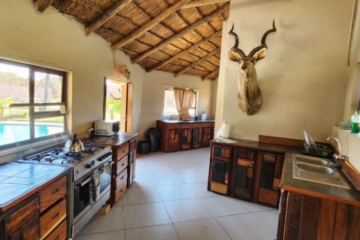 Rustic kitchen featuring wooden cabinetry, tiled countertops, a gas stove, and a double basin sink under a traditional thatched roof.