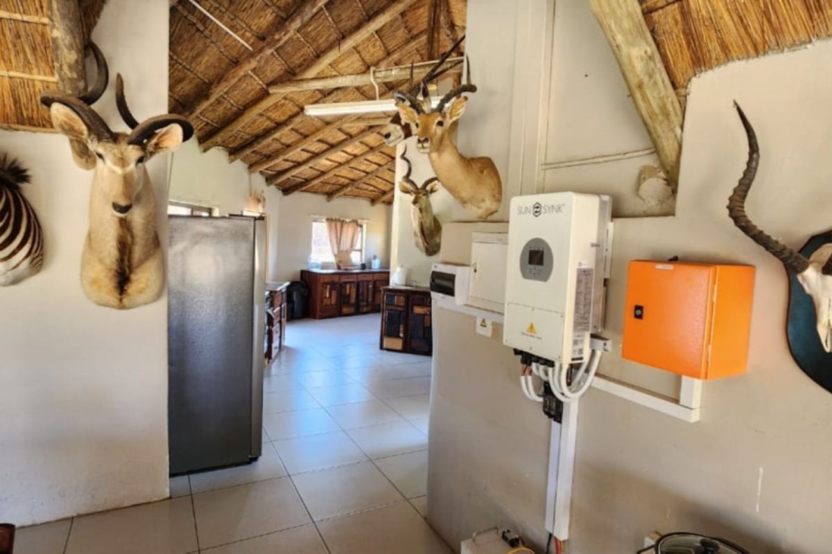 Interior view of a farm-style living area featuring a high thatched roof, tiled flooring, and wall-mounted solar inverter system.