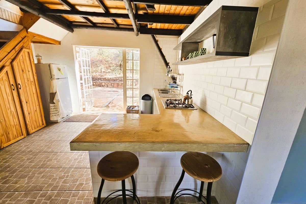 A rustic kitchen featuring a concrete breakfast bar, subway tile backsplash, exposed timber ceiling beams, and direct access to an outdoor patio area.