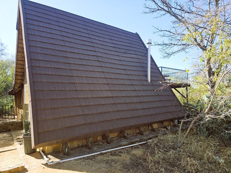 A side view of an A-frame house featuring a steep tiled roof, a metal chimney flue, and a raised balcony area.