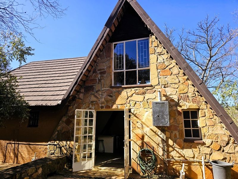 A rustic A-frame house featuring natural stone cladding, a steep pitched roof, and French door access to the interior living space.
