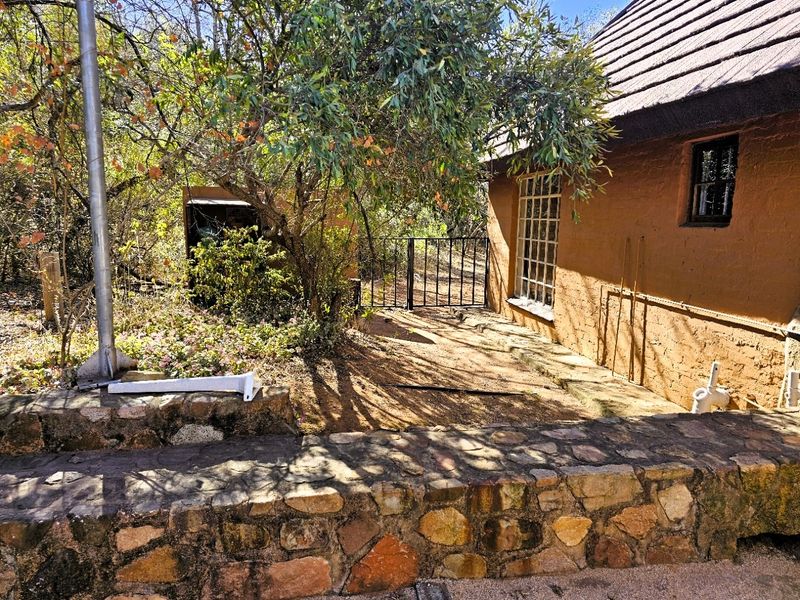A rustic exterior view featuring a stone retaining wall, textured earth-toned facade, and a metal security gate leading to a secluded garden area.