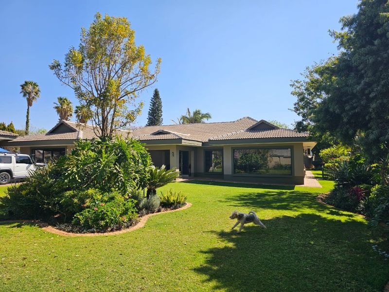 A well-maintained single-story residential home featuring a tiled roof, large windows, and a spacious, landscaped front garden with established trees and lawn.