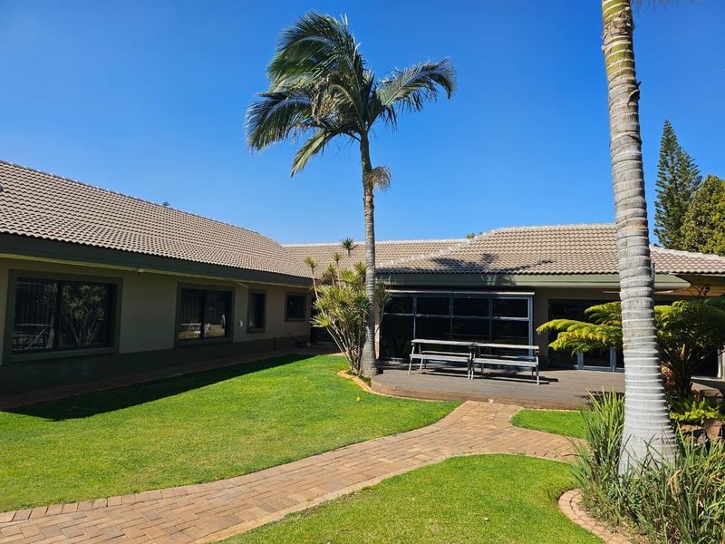 A well-maintained rear garden featuring a paved walkway, manicured lawn, and a wooden deck area attached to the house.
