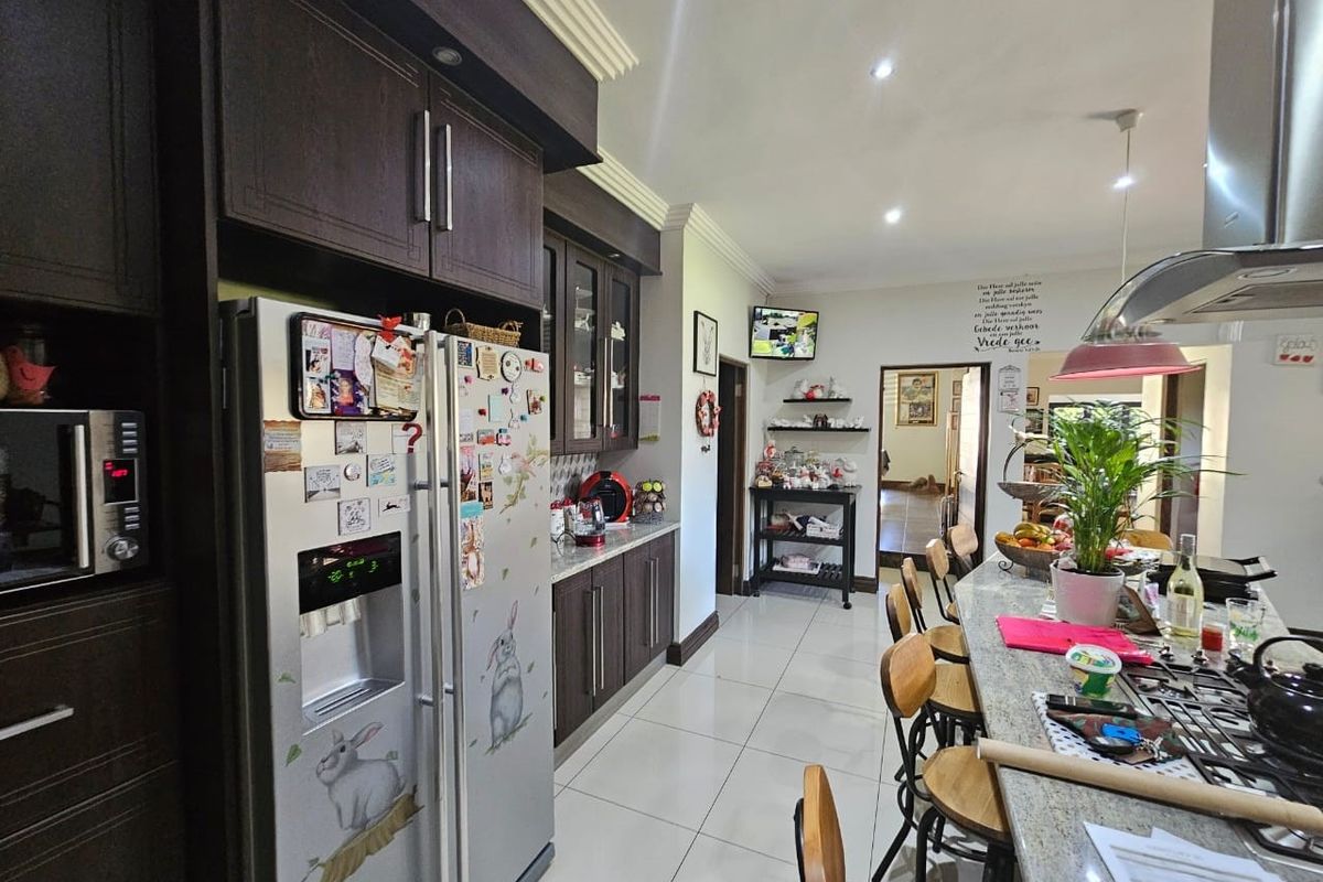 A functional kitchen featuring dark wood cabinetry, granite countertops, a breakfast bar, and tiled flooring, seamlessly flowing into the adjacent living area.