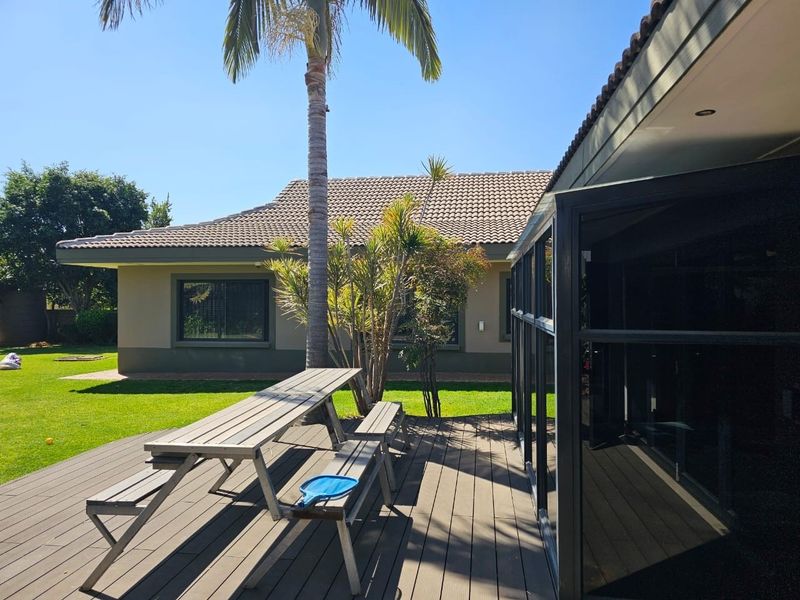 A spacious outdoor timber deck area featuring a covered patio section, overlooking a well-maintained garden and the rear elevation of the house.
