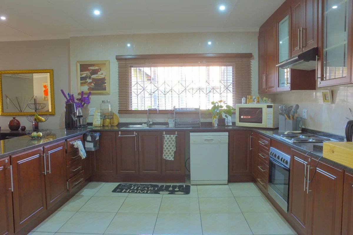 A functional kitchen featuring dark wood cabinetry, granite countertops, tiled flooring, and integrated appliances including an oven, hob, and extractor fan.