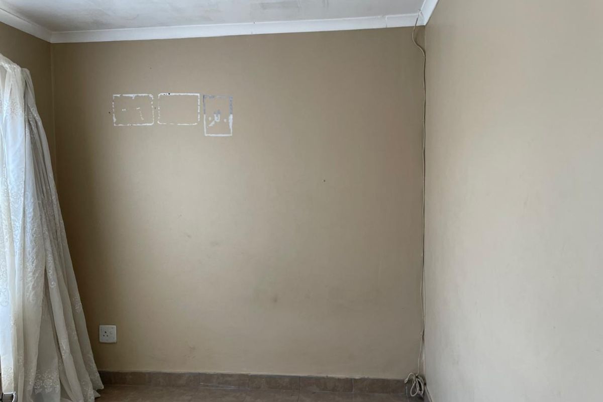 A bedroom interior featuring tiled flooring and wall surfaces showing signs of wear and previous fixture removal.
