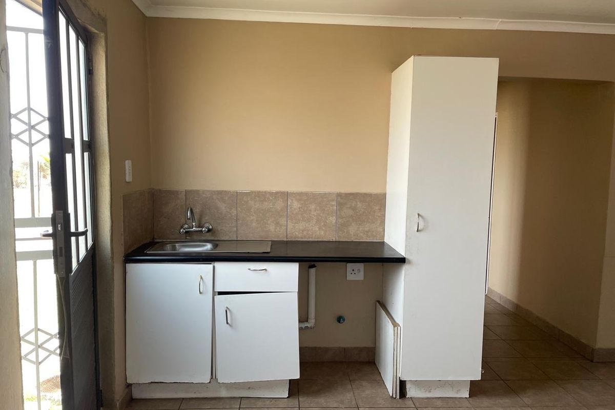 A compact kitchen area featuring a single sink, laminate countertop, and built-in cabinetry with tiled flooring and splashback.