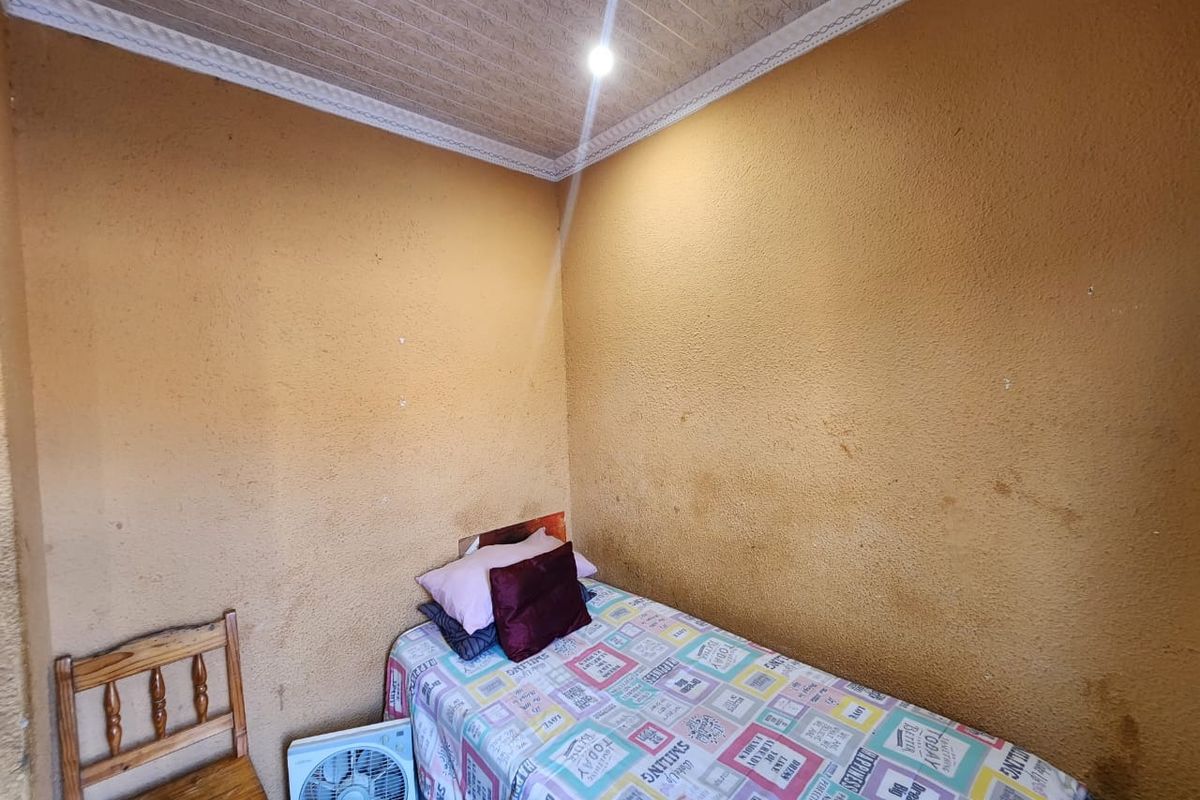 A compact bedroom featuring textured ceilings with decorative cornicing and walls showing signs of wear and staining.