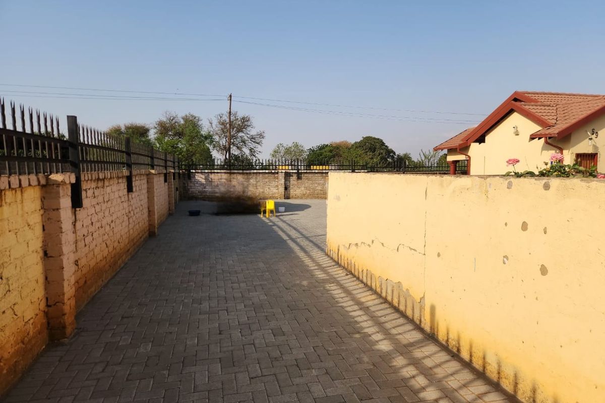 A paved rear exterior area enclosed by high brick perimeter walls with security spikes, showing signs of weathered plaster and paint.